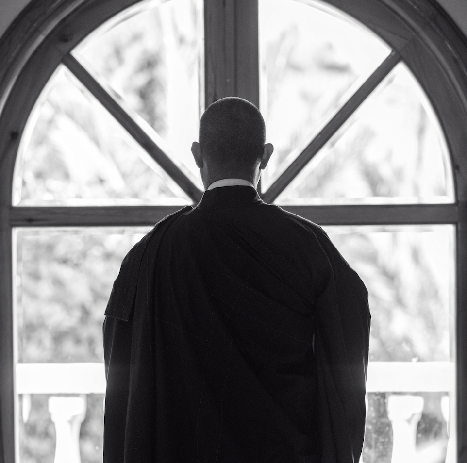 A man in robes looking out an arched window